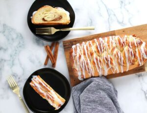 Cinnamon Butter Braid Pastry next to two plates with pastry slices, forks, and cinnamon sticks